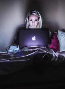 woman in bed using her laptop Disinhibition Effect in Online Therapy - a woman sitting in bed using her laptop